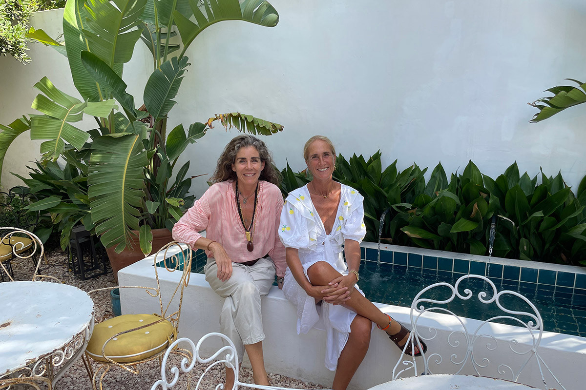 Maria Escardo and Cristine Bedfor sitting in the garden of Hotel Cristine Bedfor looking at the camera.